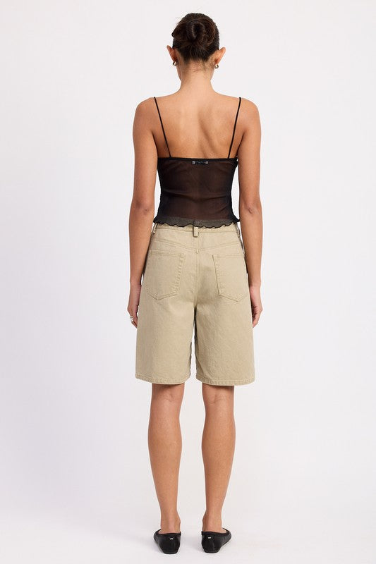Back view of model wearing sheer mesh floral cami top with thin straps paired with beige knee length shorts and black flats