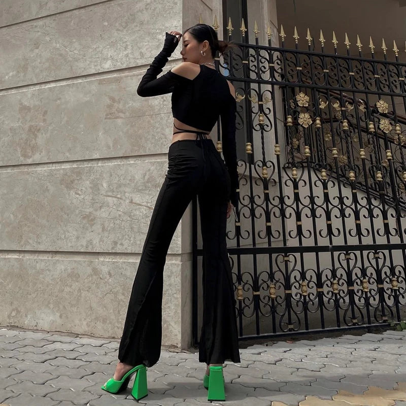 Woman wearing sheer streetwear crop tee for women with long sleeves and cutout shoulders paired with black pants and green heels