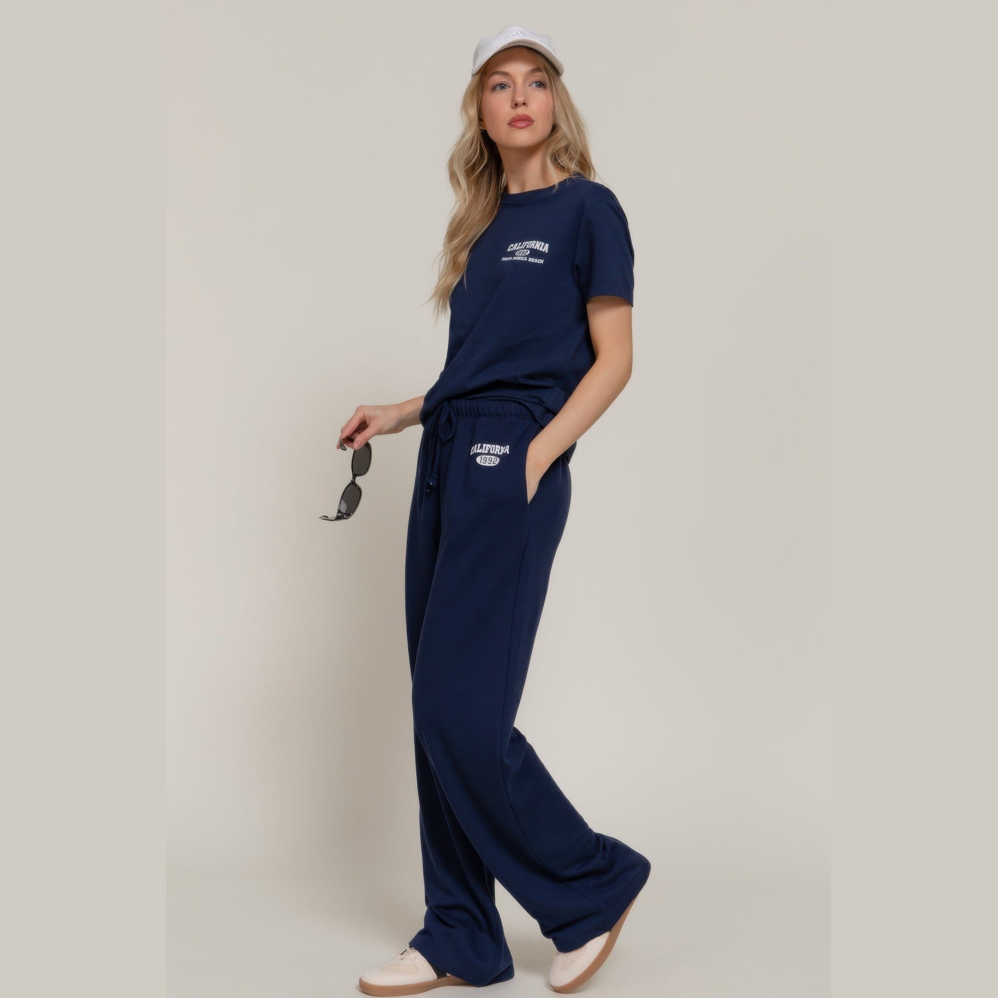 Woman wearing navy casual vacation lounge pants and matching t-shirt holding sunglasses
