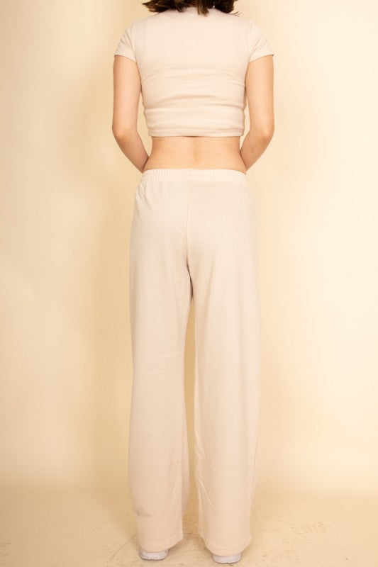 Back view of a model wearing a casual wide-leg pants outfit by Capella in a neutral beige tone