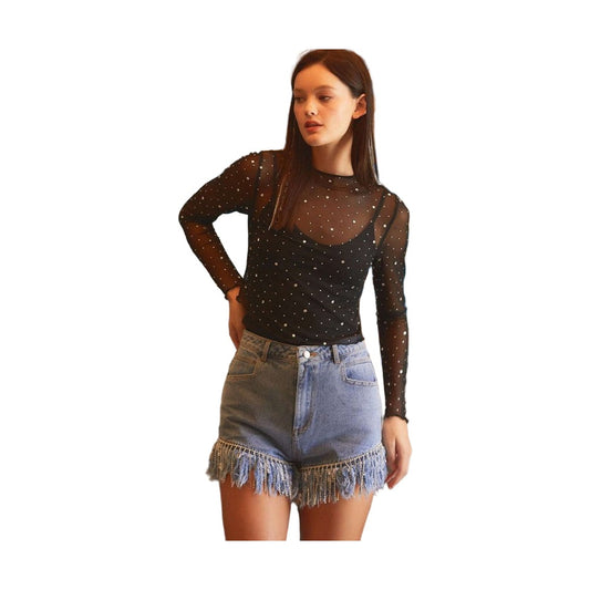 Model wearing a YNIQUE black rhinestone mesh top with long sleeves over camisole paired with fringe denim shorts