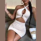 Woman wearing a white cross strap backless club dress sitting on a sofa holding a drink