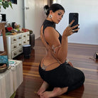 Woman wearing a black backless cut out club dress taking a mirror selfie indoors