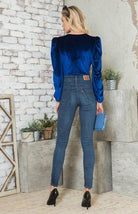 Elegant women's bodysuit in blue velvet with puff sleeves, styled with skinny jeans and high heels