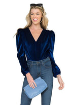 Elegant women's bodysuit in navy with puff sleeves, styled with high-waisted jeans and a blue clutch
