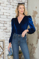 Elegant women's bodysuit in blue velvet with puff sleeves and deep V-neck, styled with high-waisted jeans