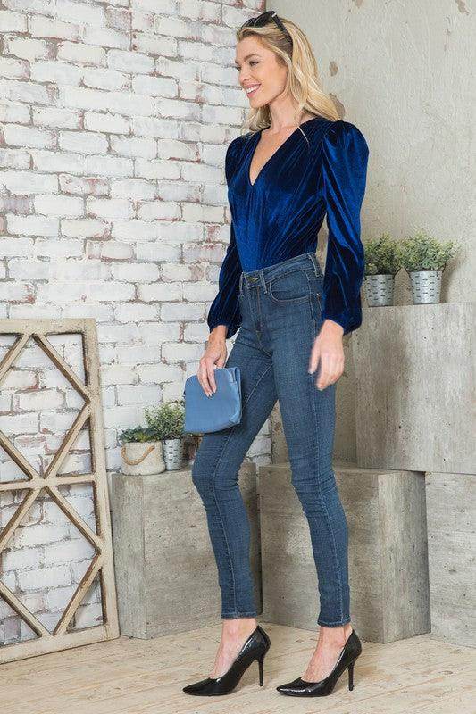 Elegant women's bodysuit in blue velvet with puff sleeves paired with skinny jeans and heels