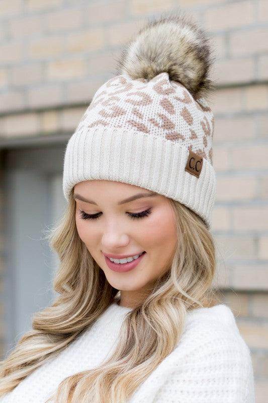 Stylish woman wearing a fashionable animal print beanie with a faux fur pom-pom from Aili's Corner