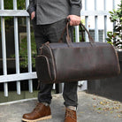 Brown foldable leather suit bag held by a man, perfect for travel and stylish storage.
