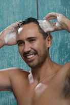 Man using a handcrafted shampoo bar while washing his hair in the shower