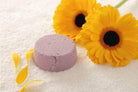 BeNat handcrafted shampoo bar in lavender color surrounded by yellow flowers and petals