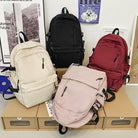 Four stylish nylon backpacks for travel in black, cream, burgundy, and light pink with multiple pockets