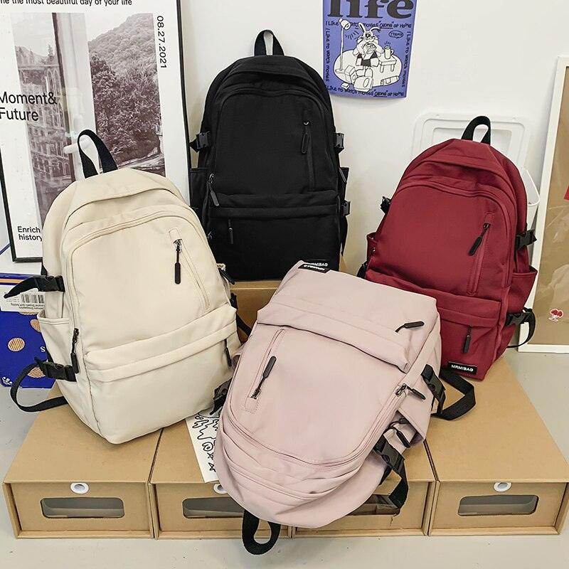 Four stylish nylon backpacks for travel in black, cream, burgundy, and light pink with multiple pockets