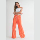 Woman wearing orange drawstring pants with white piping and a white off-shoulder top