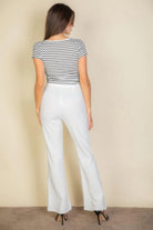 Back view of woman wearing white flare trousers paired with striped top and black heels