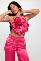 Woman wearing a pink satin crop top and wide leg pants with large floral detail on the top