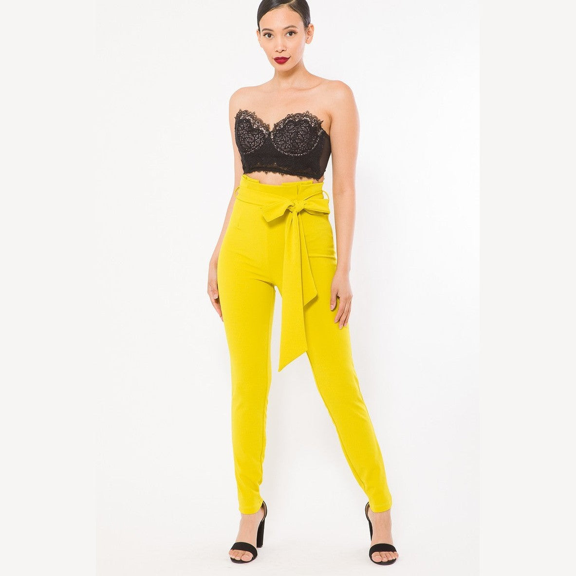Women wearing yellow skinny pants with belt accent paired with black lace crop top and heels