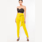 Women wearing yellow skinny pants with belt accent paired with black lace crop top and heels