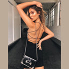 Woman wearing a black sleeveless party mini dress for women with strappy open back and silver chain purse