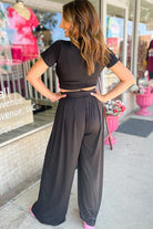 Woman wearing YNIQUE stylish summer travel outfit women with black crop top and wide-leg pants outdoors