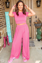 Woman wearing a stylish summer travel outfit women in a pink crop top and wide-leg pants by YNIQUE