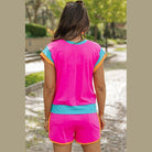 YNIQUE vibrant pink summer vacation two piece outfit with blue and orange trim on woman outdoors