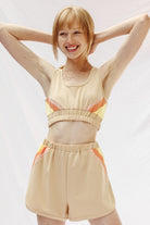 Woman wearing trendy retro activewear beige crop top and shorts with orange and yellow accents by Miss Sparkling