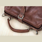 Brown leather unisex shoulder bag for travel with durable handle and metal accents
