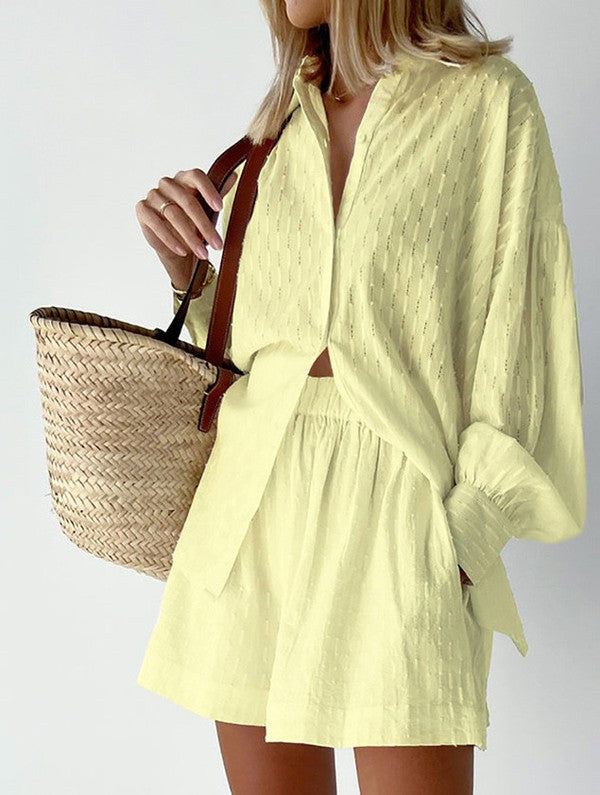 Woman wearing light yellow loose shirt and shorts vacation outfit for women holding a woven straw bag
