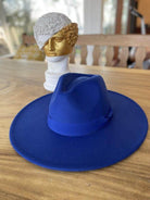 Vegan felt panama hat in vibrant blue color placed beside a decorative bust on a wooden table