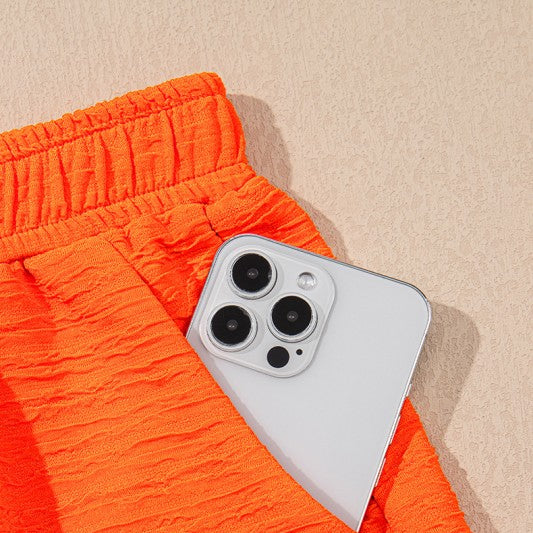 Close-up of bright orange textured pants pocket with white smartphone for casual vacation outfit for women