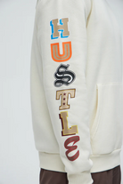 Cream hustle daily hoodie for vacation with colorful bold lettering on sleeve by VacationGrabs