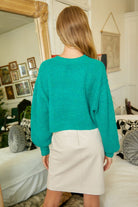 Back view of woman wearing mustard seed teal trendy sweater tops for women with beige skirt indoors