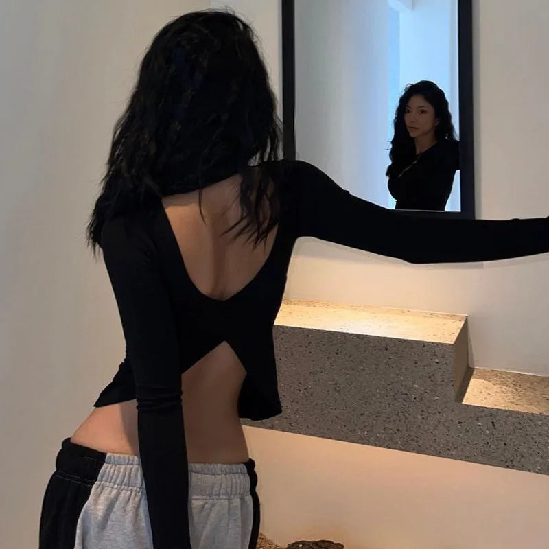 Woman wearing black backless crop top for women with long sleeves standing in front of mirror