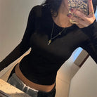 Woman wearing a black backless crop top for women with long sleeves taking a mirror selfie