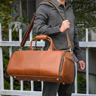 Brown foldable leather suit bag with adjustable shoulder strap for travel convenience