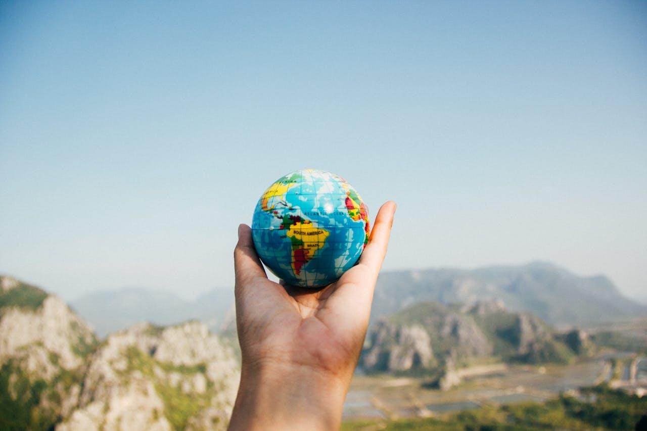 A person holding a globe against a scenic mountain backdrop, symbolizing travel advice for beginners