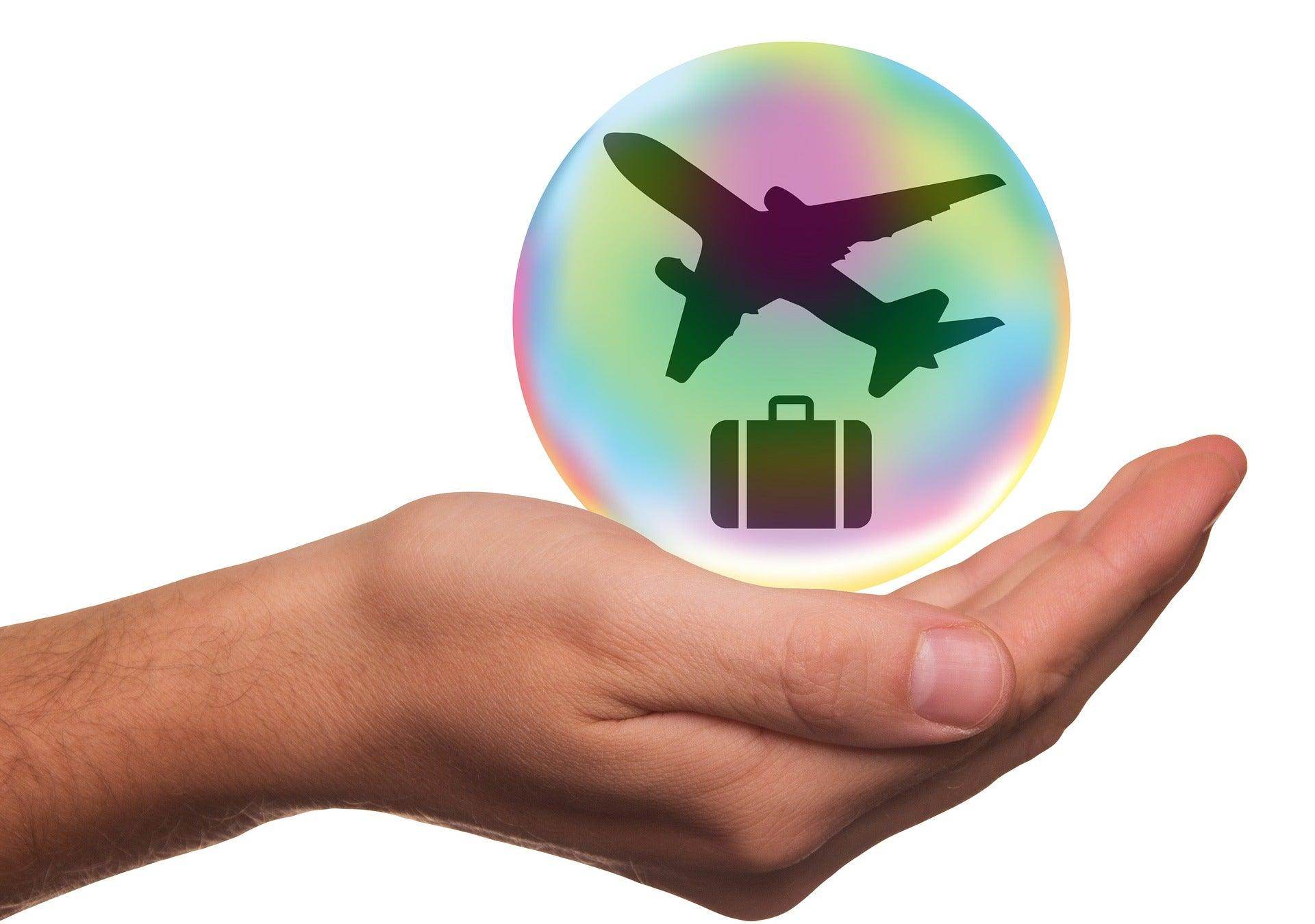 Hand holding a bubble icon with an airplane and suitcase symbolizing travel insurance for vacations