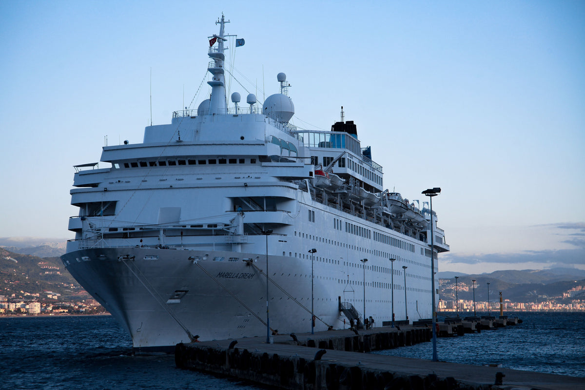 Large white cruise ship docked at a Mediterranean coastal harbor at dusk