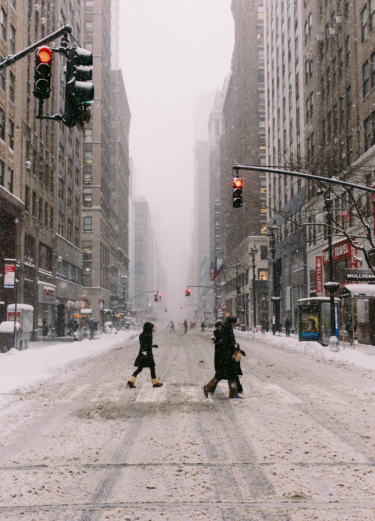 People in winter coats crossing a snowy city street during a snowstorm
