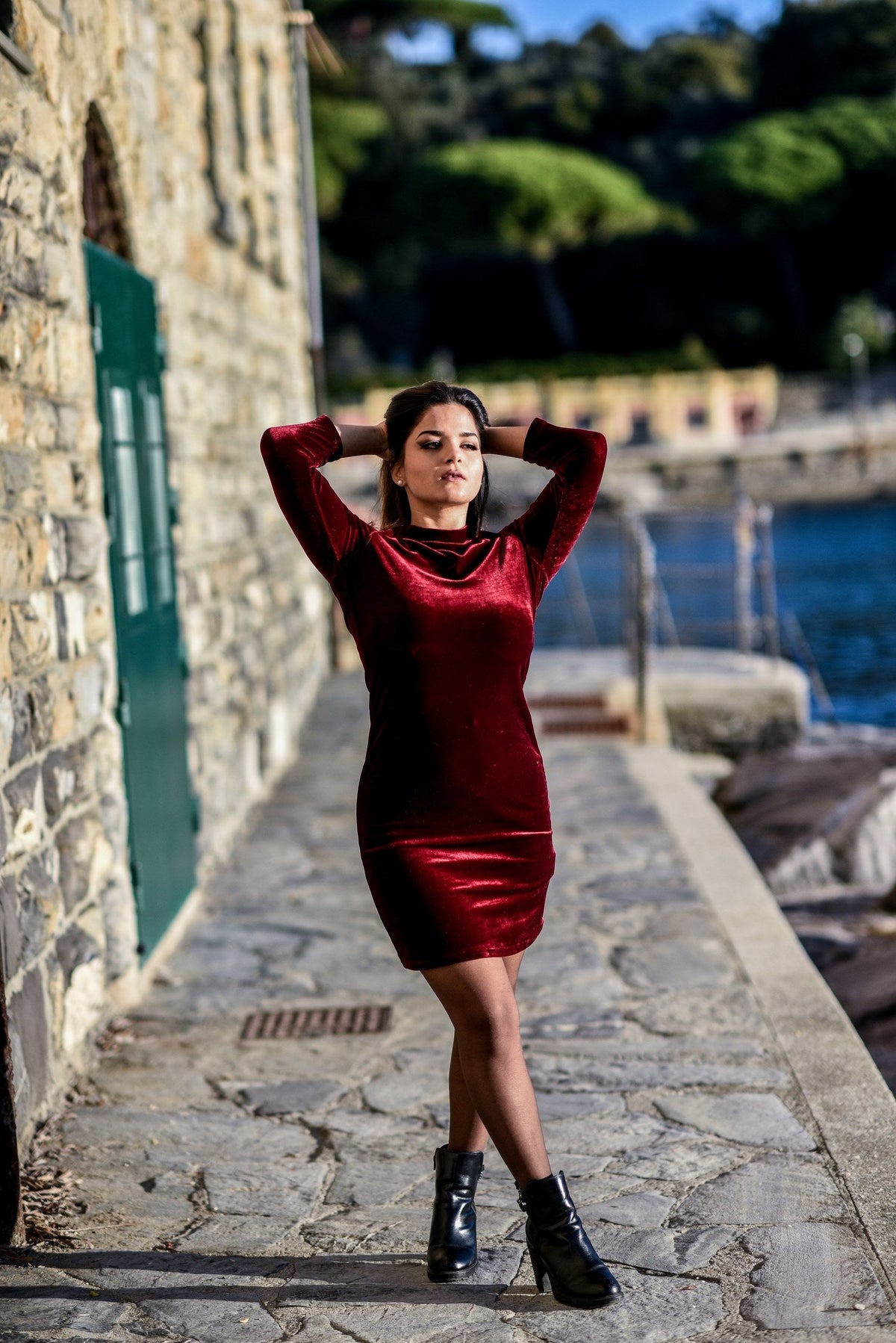 A woman in a red velvet dress posing outdoors by a stone wall
