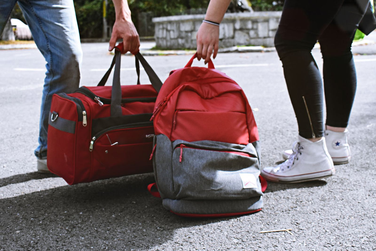 Red duffel bag and backpack being carried on a city street