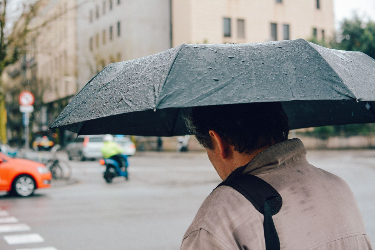 Folded black packable travel umbrella in use on a rainy city street
