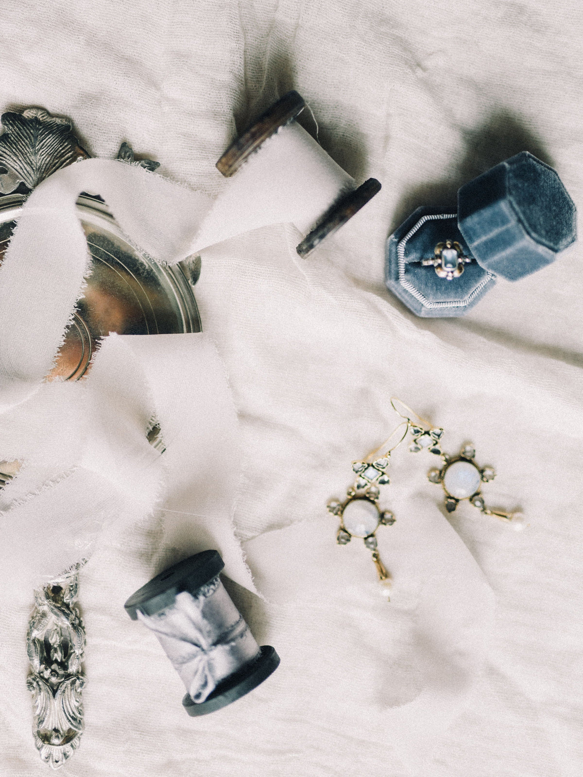 Jewelry including a ring box and earrings laid out on linen fabric
