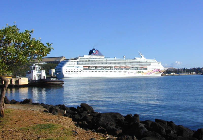 A Norwegian Cruise Line ship docked at Nawiliwili Harbor, Kauai, Hawaii, with volcanic rock coastline in the foreground. Photo: Eric Guinther, CC BY-SA 3.0, via Wikimedia Commons