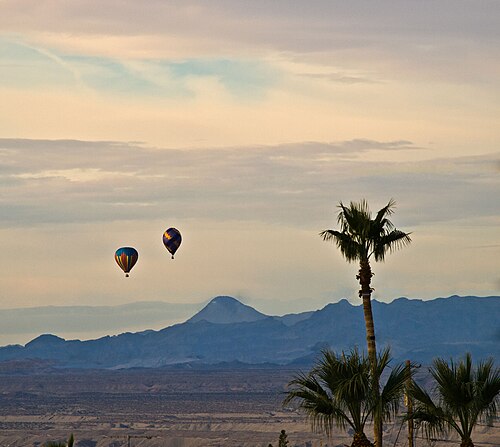 Hot air balloons floating over the Arizona desert at sunrise near mountains