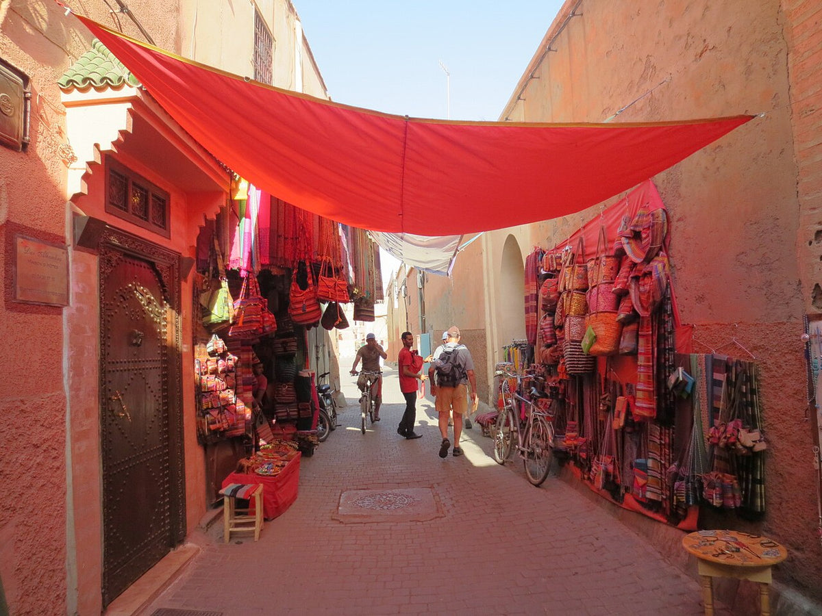 A narrow souk alley in the Marrakech medina hung with red fabric and lined with leather bags and textiles
