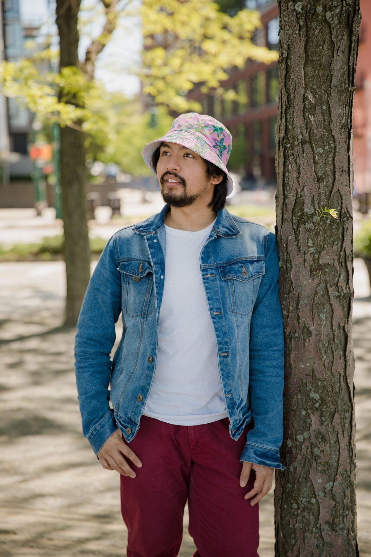 Man wearing a floral bucket hat and denim jacket outdoors in a park