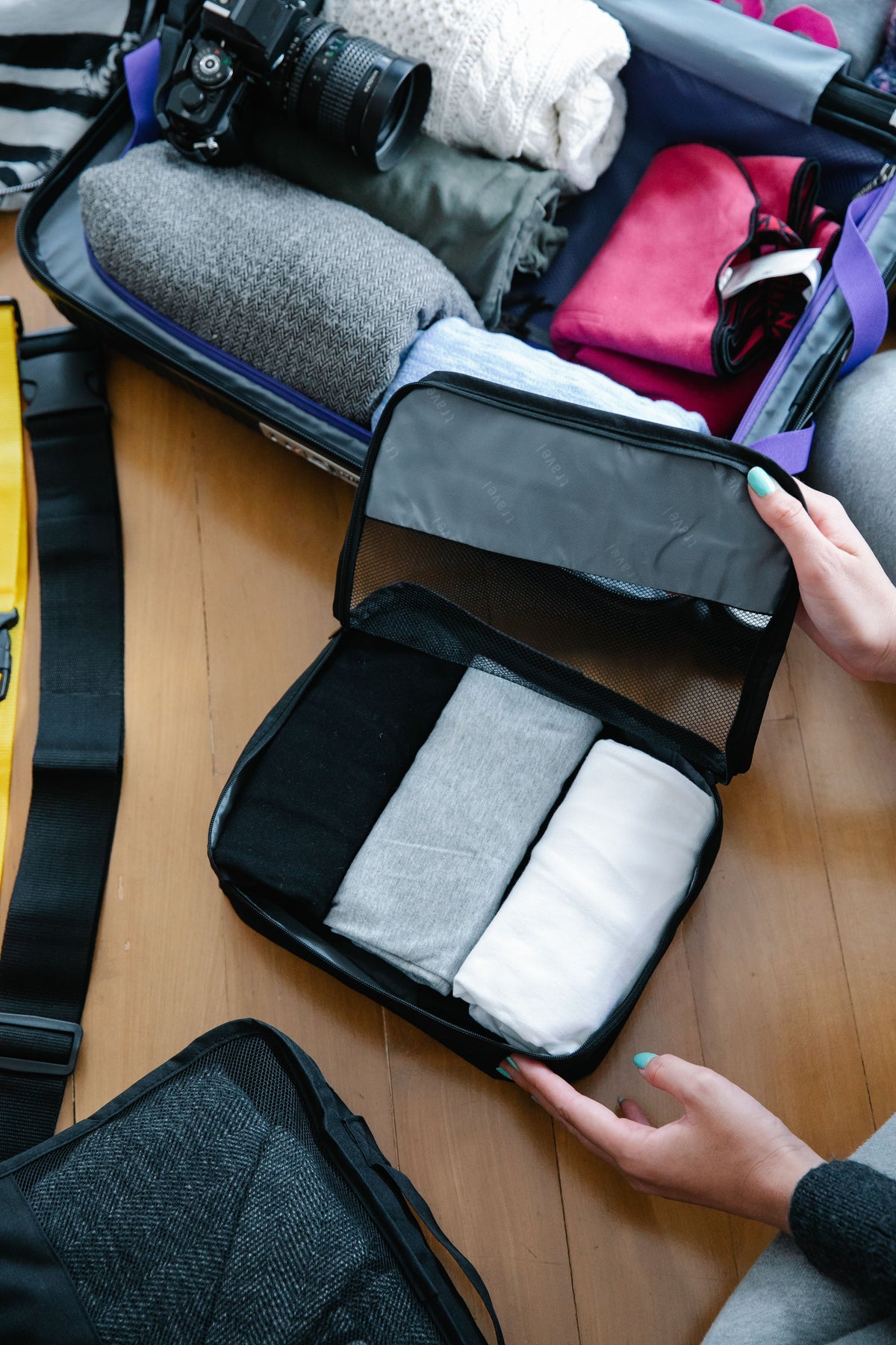 Open packing cube filled with folded clothes next to a suitcase on a wood floor