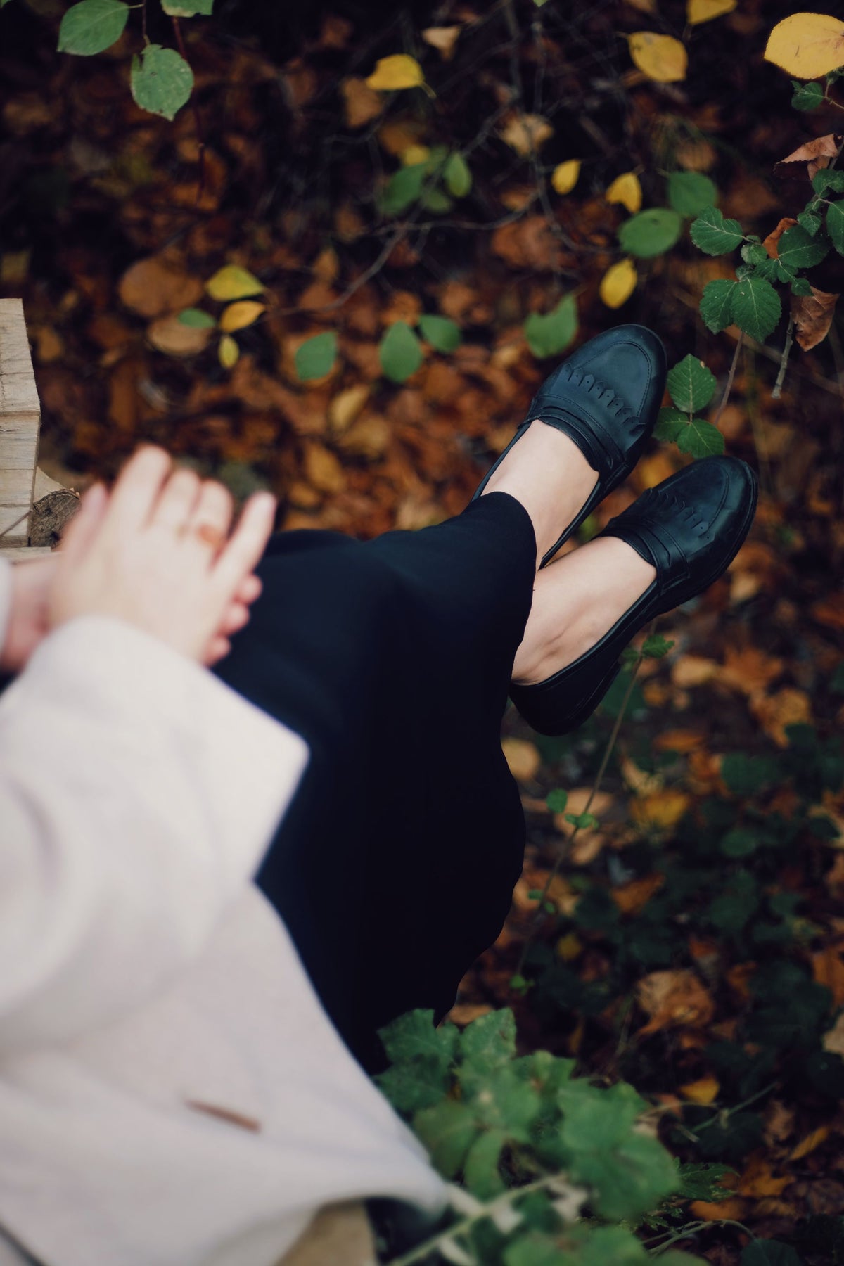 Women's black loafers, feet raised in autumn leaves
